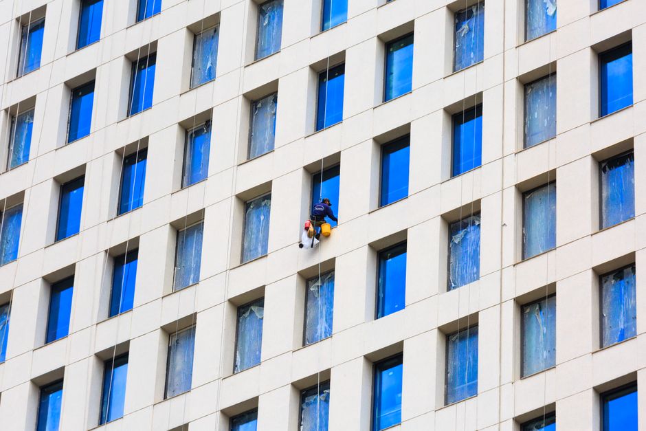 A worker cleaning windows on a tall building's facade, showcasing urban architecture.